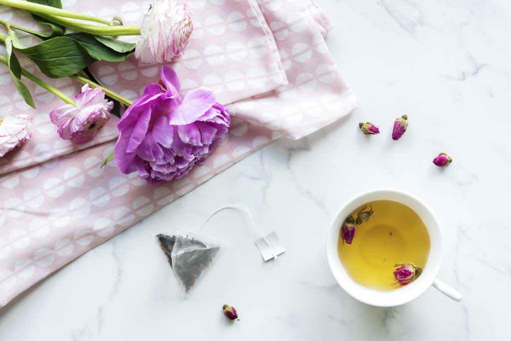 A cup of fruit tea on a marble background beside a cool-toned, soft pink flower